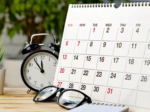 Calendário, relógio e óculos sobre uma mesa